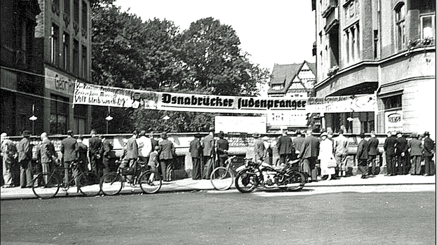 "Osnabrücker Judenpranger" in der Georgstraße. Installiert vom benachbart ansässigen Juwelier und NSDAP-Ortsgruppenführer Erwin Kolkmeyer. Auf ausgehängten Fotos waren Menschen abgebildet, die in damals noch existierenden jüdischen Geschäften gekauft hatten.